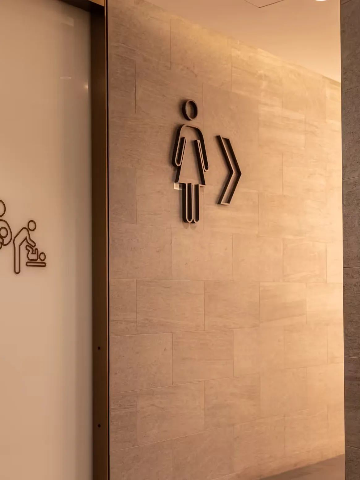 Piktogramme für Damentoilette und Wickelraum an einer Wand aus Naturstein