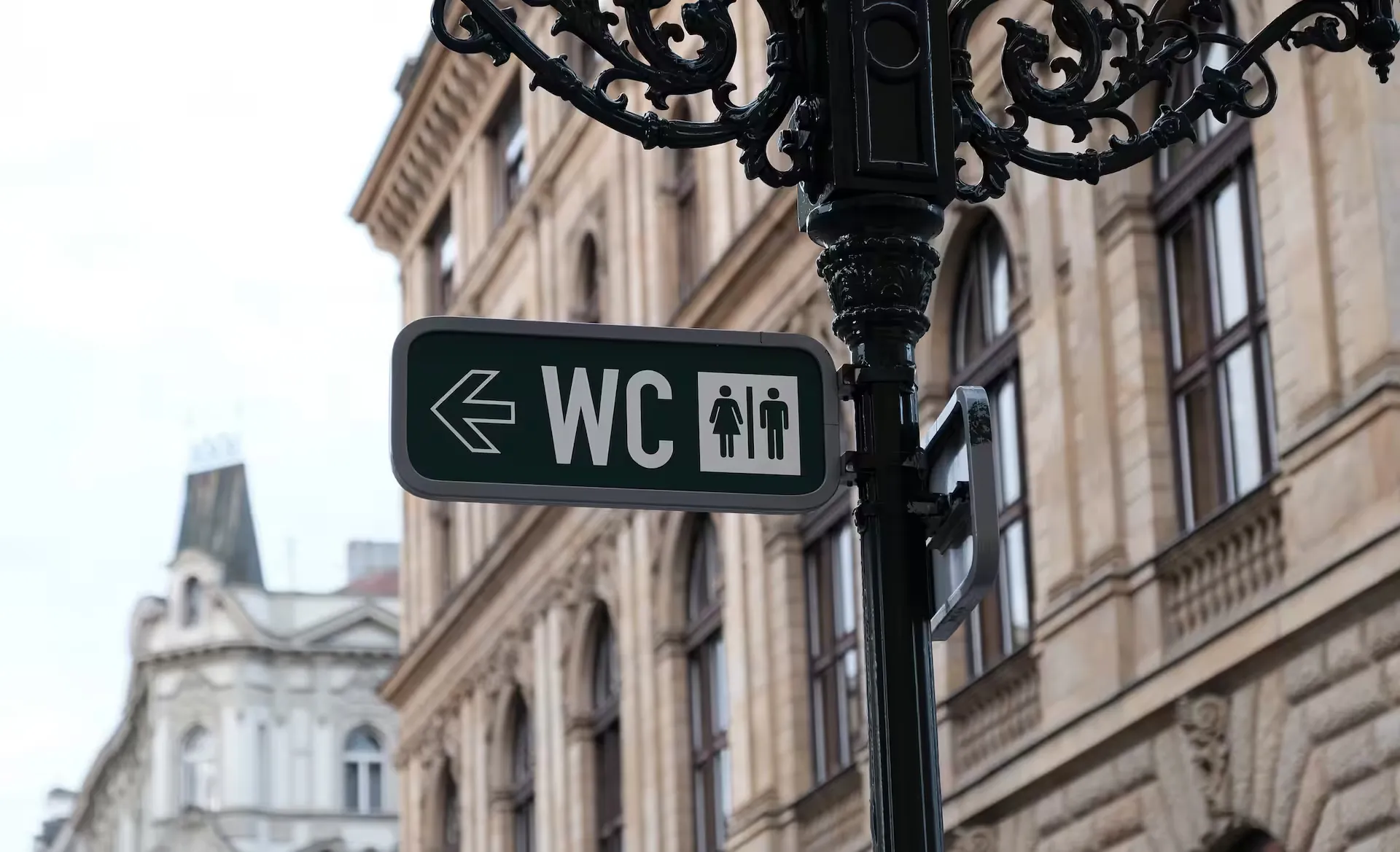 Grünes WC-Hinweisschild mit Richtungspfeil an einer Straßenlaterne vor einem Altbau